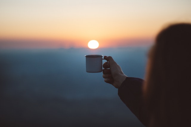 Človek s kávou v ruke pri východe slnka.jpg