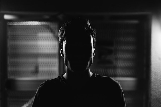 Muž s tvárou zahalenou tieňom, stojí pred oknom v tme.jpg